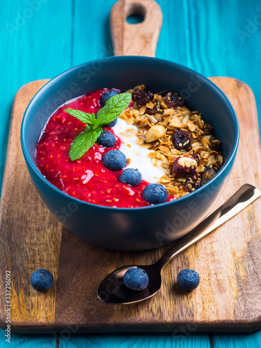 Yogurt smoothie bowl with blended raspberries, blueberries and oat matcha granola on dark green wooden background. Delicious healthy breakfast concept