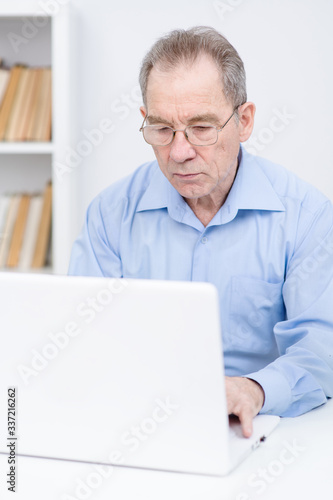An old man wearing glasses discovers on a laptop at home
