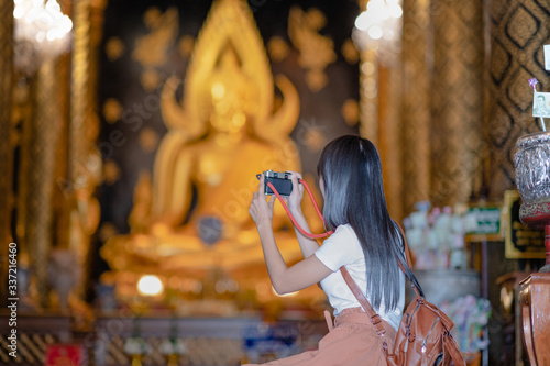 Woman traveller pay gentle respect and taking photo picture on the buddha statue in the temple, praying respect for a better life forward.