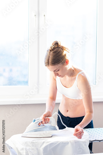 Woman Ironing Clothes Using Iron On Ironing Board After Laundry At Home