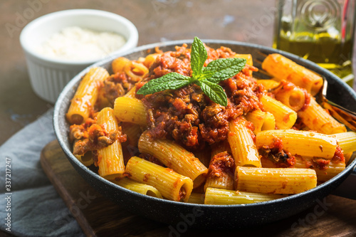 Delicious rigatoni pasta with italian tomato meat ragu sauce served in a pan on dark brown background. Traditional pasta dish concept. Home made lunch