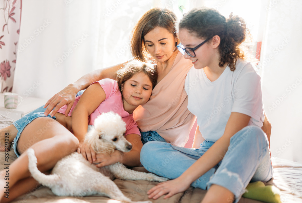 Happy family mother two daughters girls and poodle dog having fun together on bed in room at the home Happy family mother two daughters girls and poodle dog having fun together on bed in room at the home