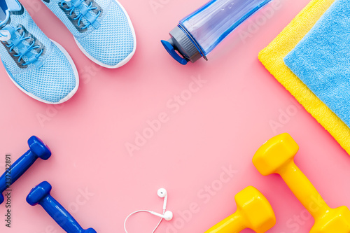 Fitness equipment. Sneakers, dumbbells, headphones on pink background top view copy space