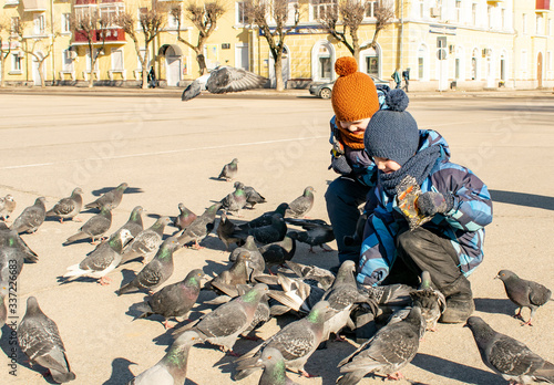 Two boys are happily feeding seeds to pigeons in the square.