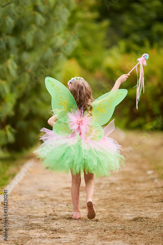 Young queen fairy with pink wings against a dark background waving a magic wand forward, fulfilling one's desires