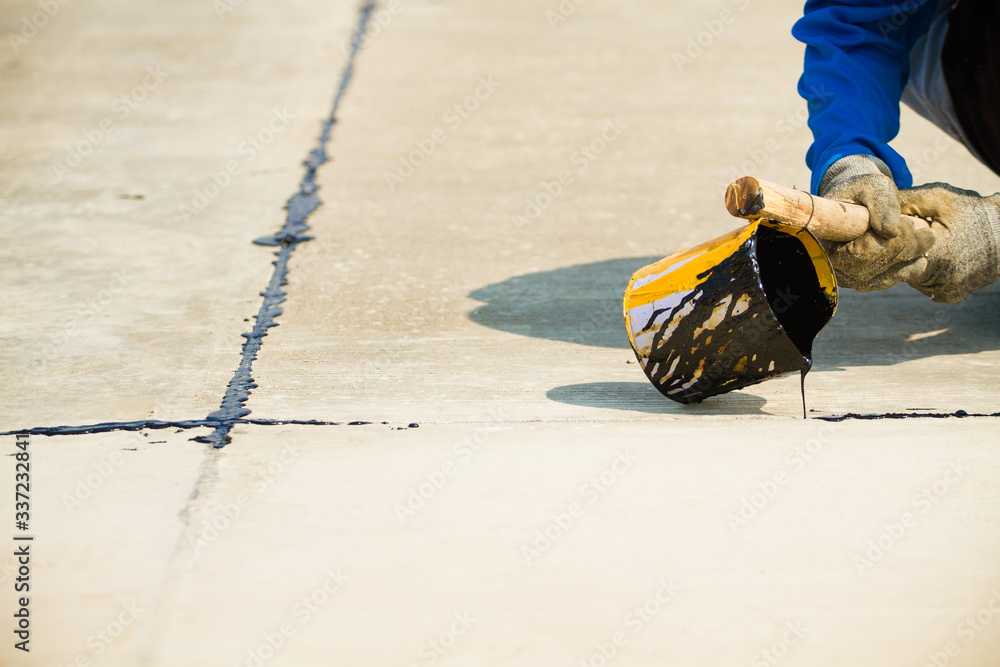 Worker sealing asphaltic joint for construction joint on concrete