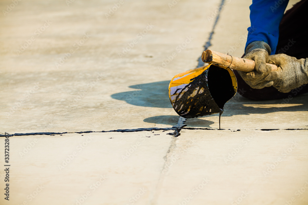 Worker sealing asphaltic joint for construction joint on concrete