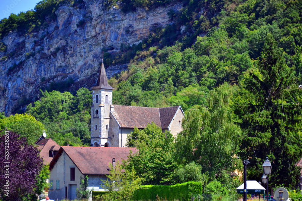 Fototapeta premium Chanaz, France - August 10th 2016 : Focus on the church of the village, very close to a big rocky mountain.