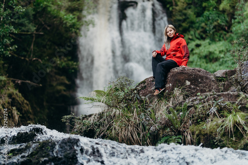 Beautiful woman hiker standing at front of waterfalls and looking away. Asian female on hike in nature.