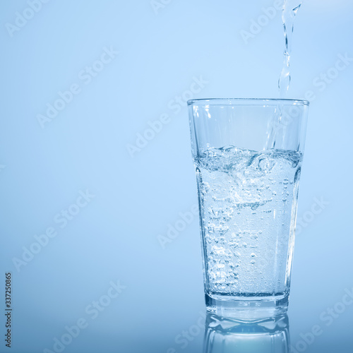 wasserstrahl beim eingießen in wasserglas vor abstraktem blauem hintergrund