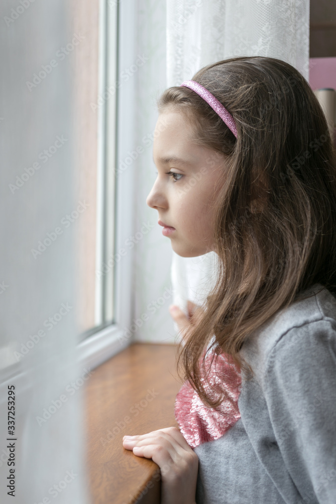 Sad, depressed and lonely little girl looking through the window. Stay home concept. Sad, depressed and lonely little girl looking through the window. Stay home concept.