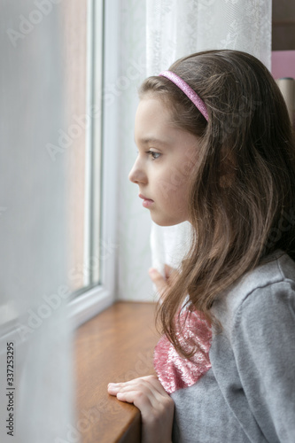 Sad, depressed and lonely little girl looking through the window. Stay home concept.
