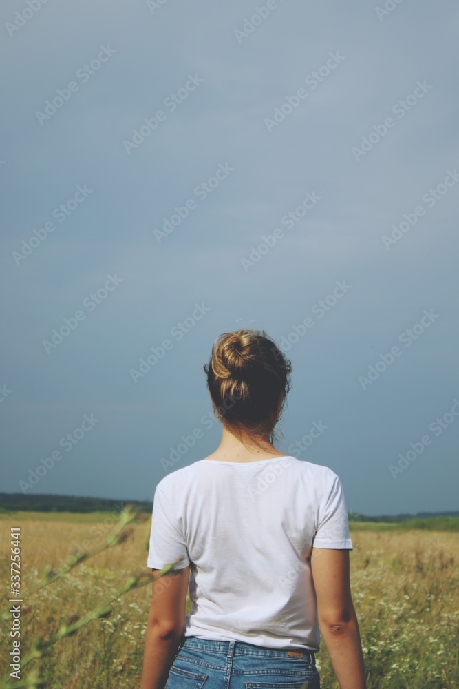 A blonde girl in white t-shirt and jeans standing in the field A blonde girl in white t-shirt and jeans standing in the field