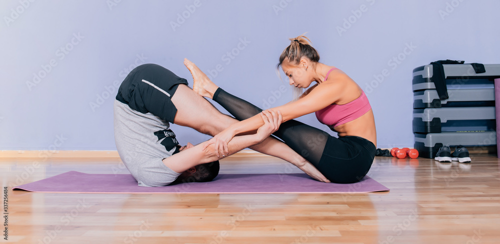 Beautiful couple in sports clothes is stretching on yoga mat while working out at home or gym. Infinite yoga pose for friends. Beautiful couple in sports clothes is stretching on yoga mat while working out at home or gym. Infinite yoga pose for friends.