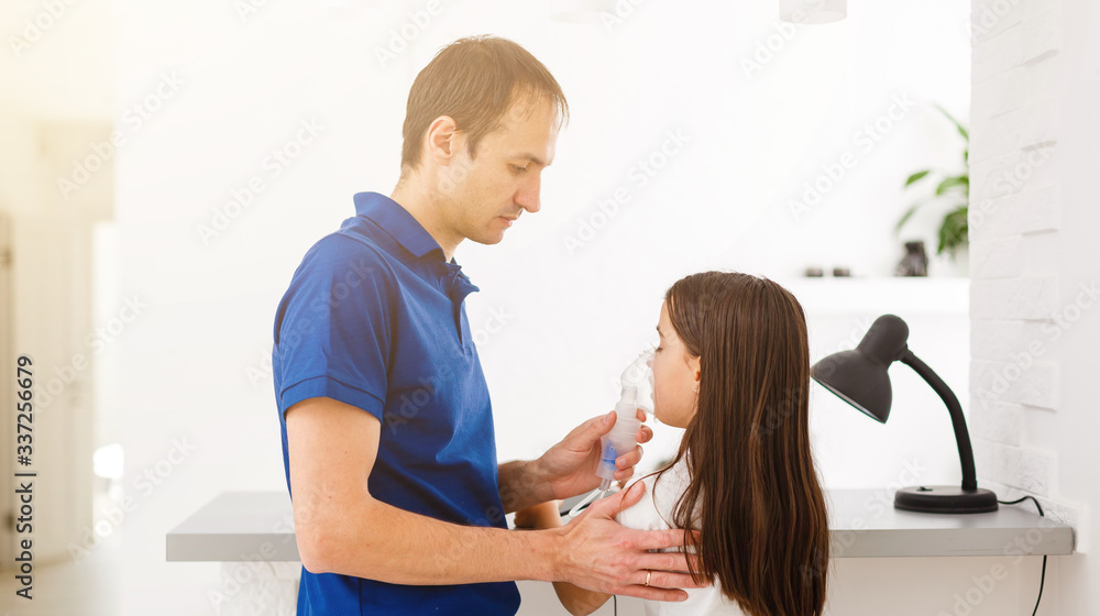 father and daughter do inhalations. caring dad helps her daughter breathe through the mask. treatment of respiratory tract. father and daughter do inhalations. caring dad helps her daughter breathe through the mask. treatment of respiratory tract.