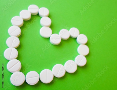 white pills on a green background in the shape of a heart. snow-white round antibiotics against viruses. photo