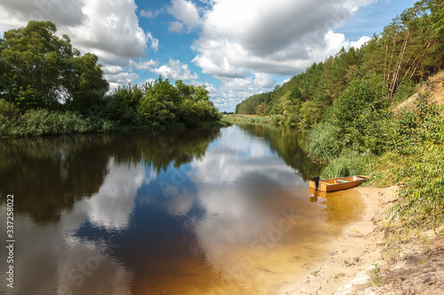 Clean river with sandy shore near the forest against a blue sky with clouds