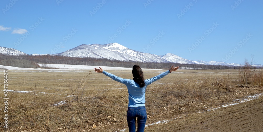 Naklejka premium Slender brunette woman embracing nature with open arms. The foot of the snowy mountains. concept of going out after quarantine. Russia, North Primorye.