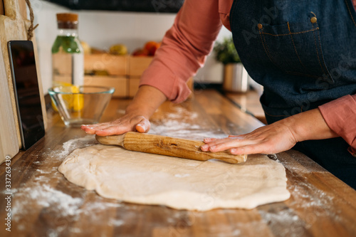 Close up of a Woman's hands rolling the dough on a wooden counter in their home kitchen. Preparation of the dough.