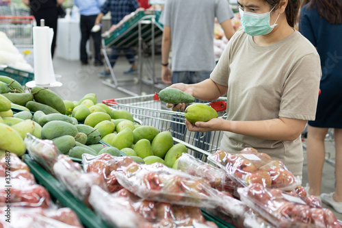 Asian woman wear a face mask,chooses necessary food,mango,fruit while shopping at supermarket,people panic buying, hoarding during the Covid-19,Coronavirus spread,girl preparing for pandemic,stay home