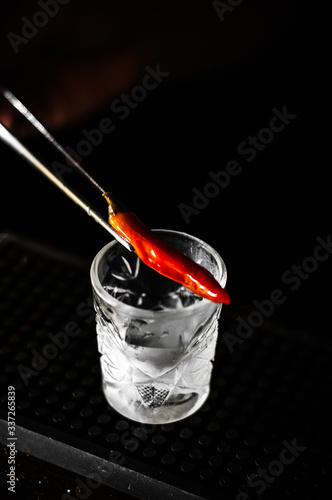 Bartender preparing exotic spicy alcohol cocktail with chili peppers at bar on black background