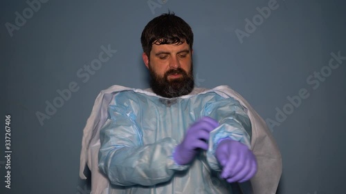 A tired doctor takes off his protective medical suit during a coronavirus pandemic. A sweaty doctor removes a medical mask and gloves at the end of the shift.