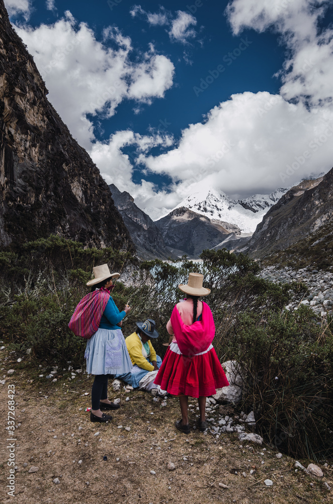 Fototapeta premium Ancash, Peru, July 29, 2014: three Peruvian women in traditional dress in the paron lagoon with snowy pyramid mountain in the background, in the andes