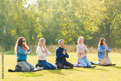 A group of young people meditate outdoors in a park. 