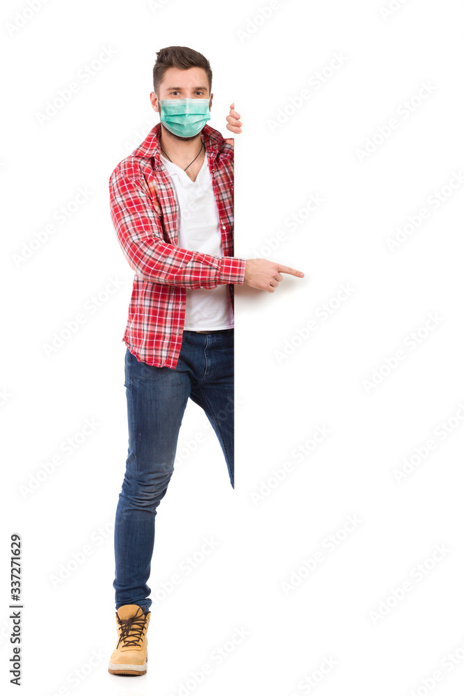 Young man wearing face mask is standing behind white banner and pointing Young man wearing face mask is standing behind white banner and pointing