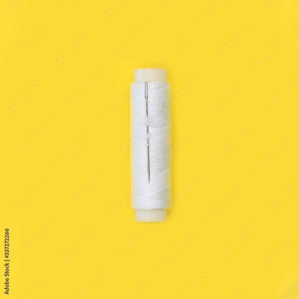 Spool of white thread with a needle on a yellow background Spool of white thread with a needle on a yellow background
