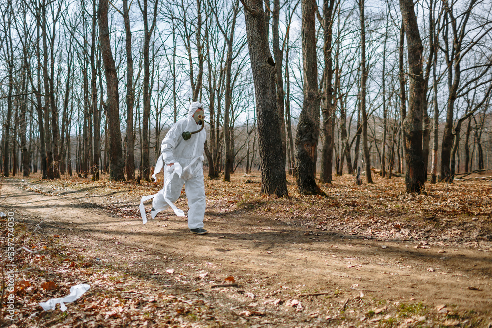 Fototapeta premium A man in a sanitary suit and a gas mask is Jogging in the woods. The suit is tied with toilet paper