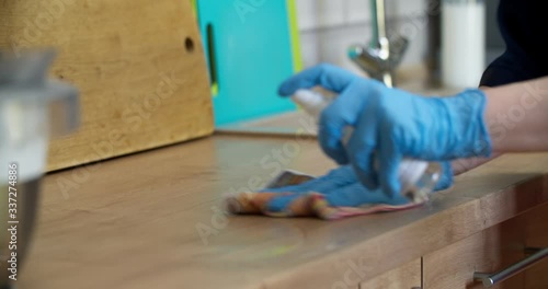 A woman treats the surface of a countertop with an antiseptic spray. Disinfecting the surface of your own kitchen. Woman in gloves cleaning