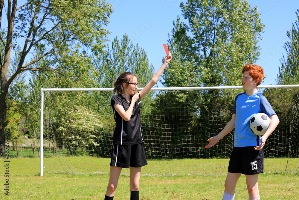 A teenage girl soccer referee sending off a teenage boy during a football game.