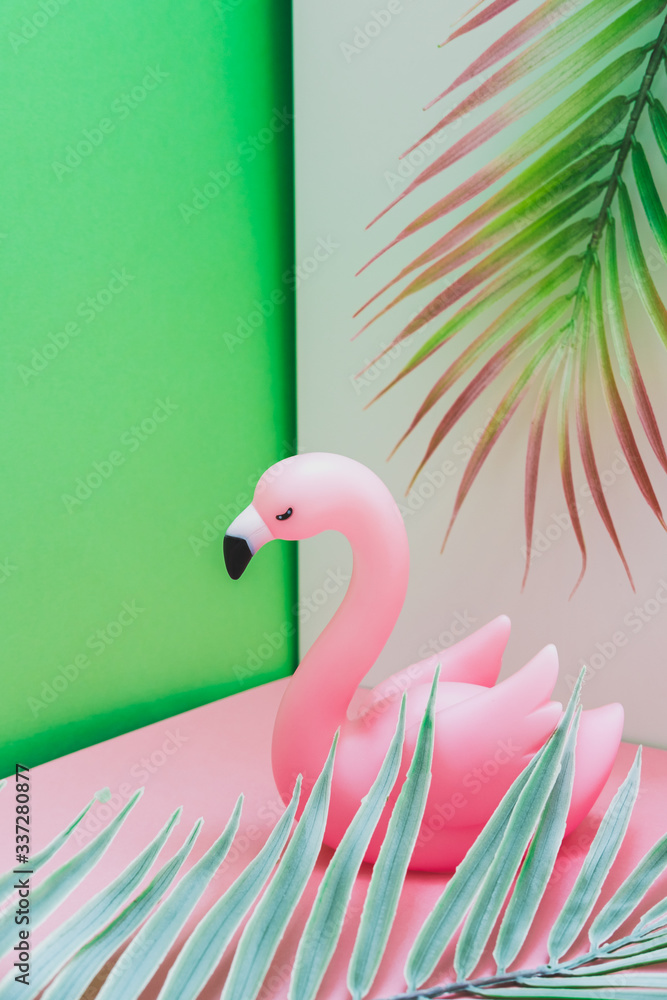 Obraz premium Plastic flamingo in the pink and green corner with palm leaves. Hot summer vacation concept in tropical style.