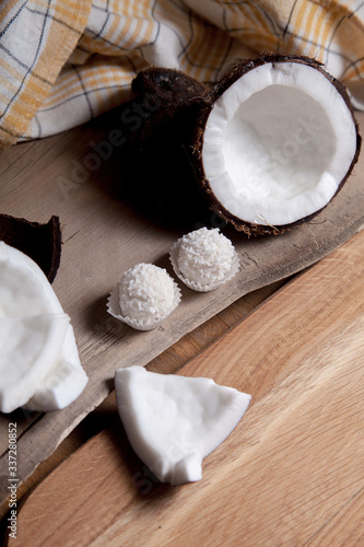 Coconut with white pulp and white candies on wooden background..