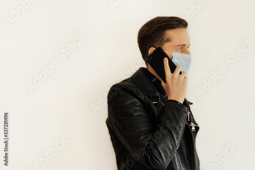 Side view of serious brunette man with surgical medical mask using cell phone. Indoor studio shot on white background. Copy space for advertising. Coronavirus pandemic.
