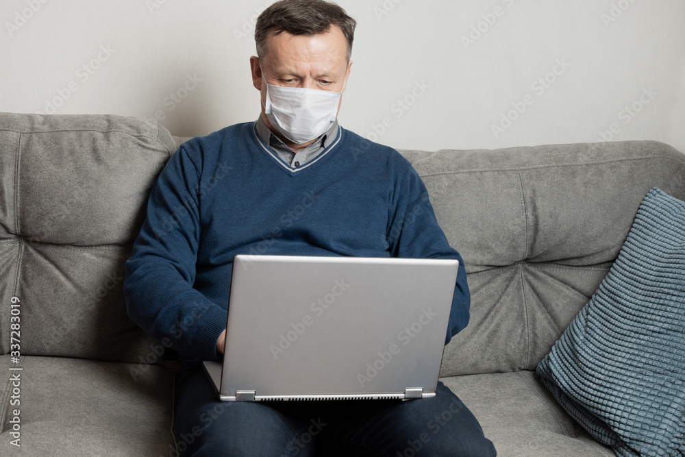 Adult man in protective medical mask work at home by laptop. Remote work. Covid-19. Quarantine. Stay at home. Adult man in protective medical mask work at home by laptop. Remote work. Covid-19. Quarantine. Stay at home.