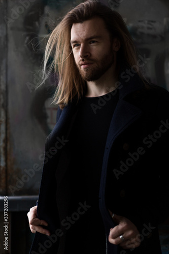 Portrait of a young handsome man. Long brown hair, beard, blue eyes, 30 years old. A man is sitting under a bridge