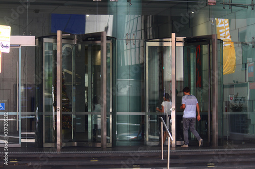 Revolving door entrance to glass modern office building in the city. Pictured are two people walking though the glass doors. 135 King street, Sydney