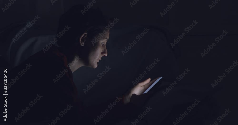 Woman with cellphone lying in bed, browsing in night Woman with cellphone lying in bed, browsing in night
