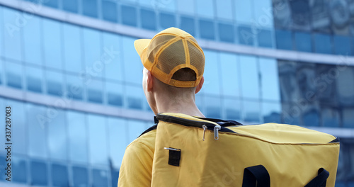 The courier in yellow uniform with a thermo backpack on the background of a business center with blue windows.
