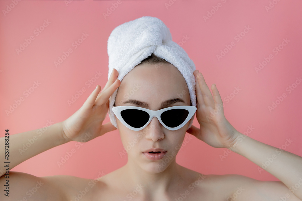 Beautiful young woman in glasses with a towel on her head after bath on pink background Beautiful young woman in glasses with a towel on her head after bath on pink background