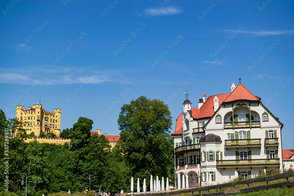 View of a beautiful white-fronted mansion in contrast to the beautiful Hohenschwangau castle from the hill. Photograph taken in Schwangau, Bavaria Germany.
