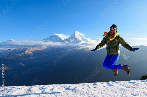 Girl is jumping in front of the mountains. White clouds. Green forest.