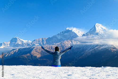 Girl is sitting in front of the mountains. White clouds. Green forest.