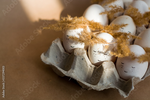 Happy Easter and white eggs in corton tray with cute faces in wreaths made of spikelets.