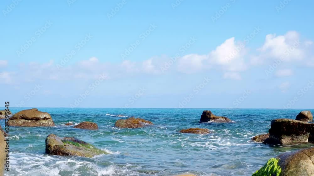 Sea waves in summer time. Clear blue sky and nice clouds over the horizon. Water waves splashing over rocks and stones in the beach shore. Sea waves in summer time. Clear blue sky and nice clouds over the horizon. Water waves splashing over rocks and stones in the beach shore.