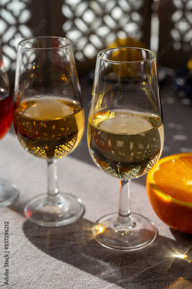 Glasses with cold dry fino and sweet cream sherry fortified wine and orange in sunlights, andalusian style interior on background