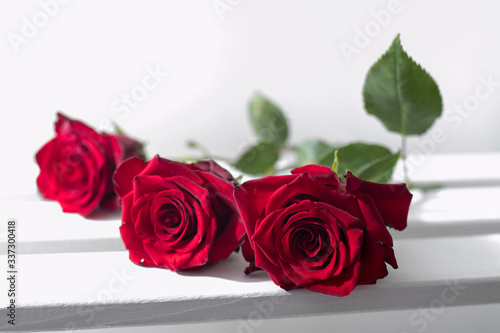 Three dark red roses lie on a wooden box. Two crystal glasses with champagne in defocus.