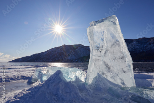 A huge block of ice sticks out of the ice against the background of the sun and mountains